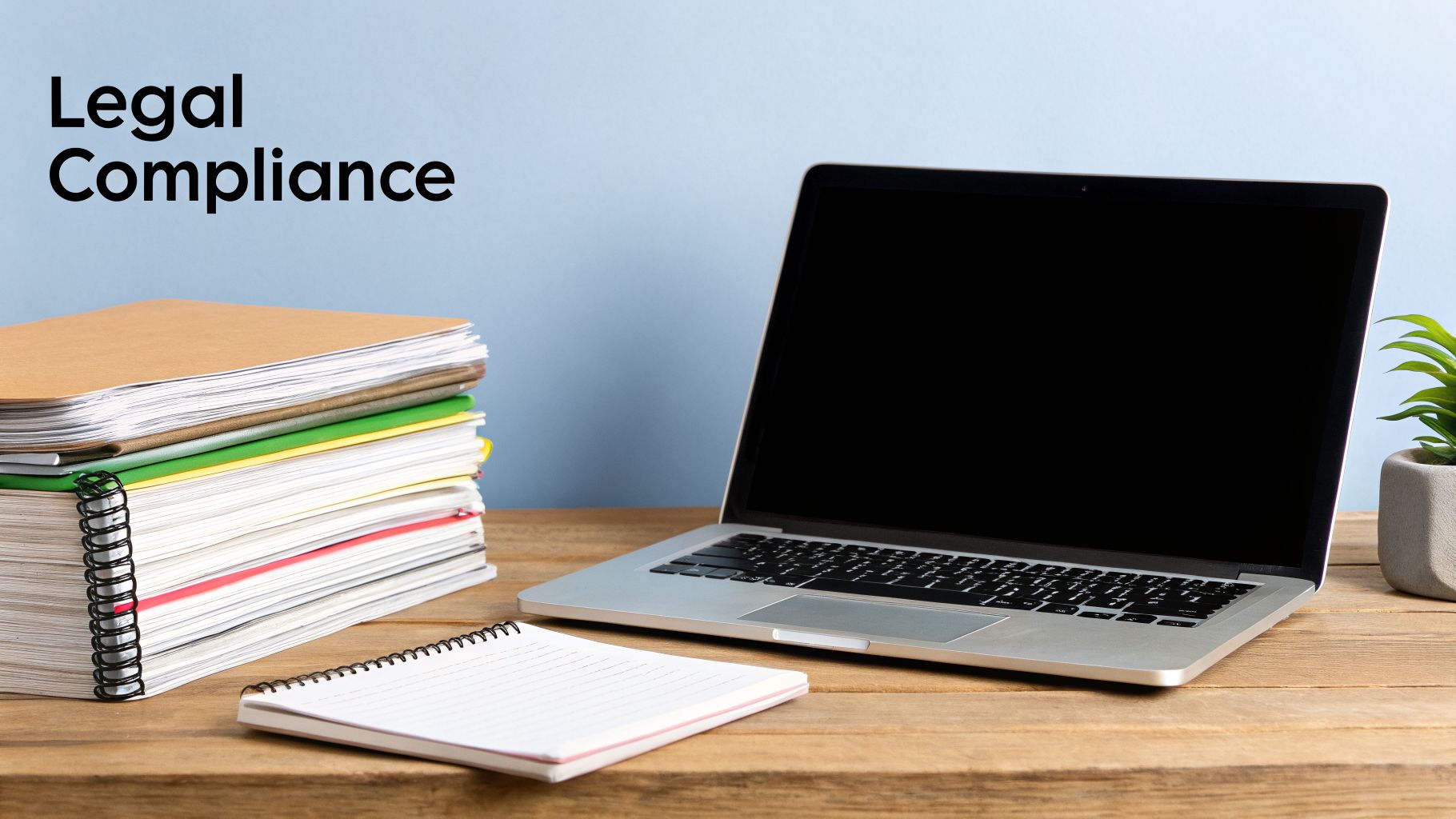A desk setup with stacked legal files, an open laptop, and a notebook, featuring 'Legal Compliance' text.