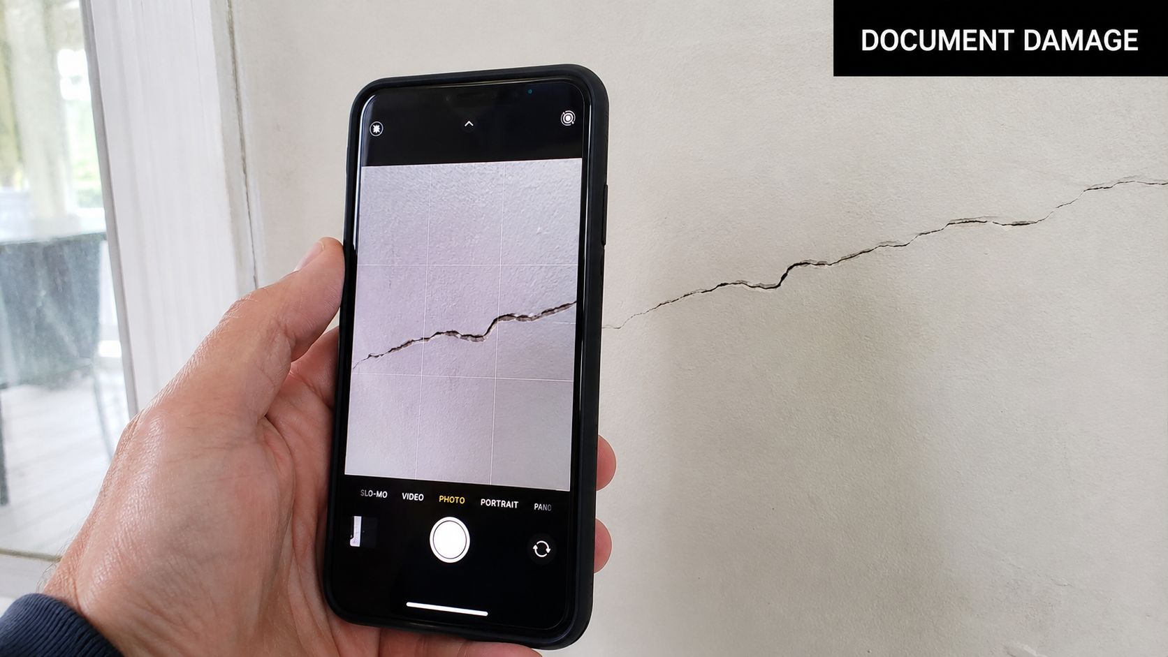 A person uses a smartphone to capture a photo of a crack in an indoor house wall.
